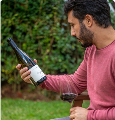 Eduardo Araújo segurando taça e lendo rótulo do vinho